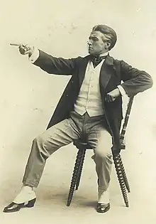 A young Claude Rains dressed as a lawyer, sitting on a chair and pointing