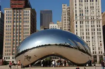 A large, highly-polished, mirrored bean-shaped sculpture seen from the east, reflecting the skyscrapers to the north along East Randolph Street (The Heritage, Smurfit-Stone Building, Two Prudential Plaza, One Prudential Plaza, and Aon Center.