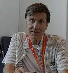 Milligan seated, wearing a lanyard and looking to the camera