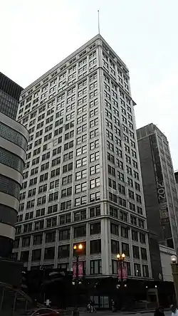 Looing up at a tall grey stone building covered with windows.