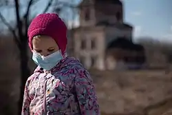 Young girl looking down, wearing a with a pink beanie, floral puffer and a surgical mask