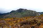 Scruffy, rocky ridge overlooking a hill covered in golden-coloured grass and shrubbery