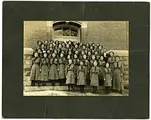 A group portrait of Girl Scouts in Crothersville, Indiana, circa 1945. The girls are gathered in rows and are standing in front of the doors of a brick building.