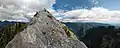 bare rock peak topped by fourteen hikers and two crows, with steep forested valleys in the background