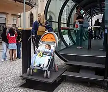 a woman with a baby carriage uses a platform lift to access a station above street level