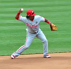 A young, dark-skinned man with dreadlocks throwing a baseball with his right hand