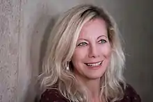 middle-aged white female with long blonde hair, grinning, looking left of camera