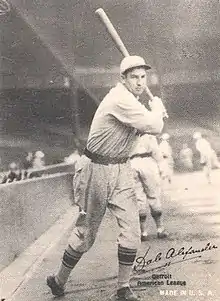 A black and white photograph of a baseball player posed with a bat swung behind his head