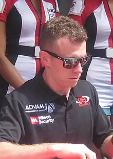 A man in his early thirties wearing black rectangular sunglasses and a black T-shirt