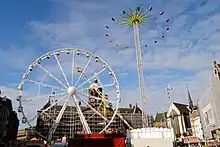 An image of the funfair in Dam square showing a Ferris wheel on the left, behind it spinning-arm ride called Speed; and a Matterhorn on the right with its spinning cars at maximum extension.