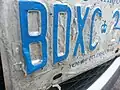 Close-up view of early damage to a front licence plate of an Ontario car. The reflective layer can be seen de-laminating and separating from the metal base.