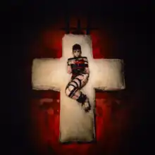 An individual wearing a dress made out of leather belts and lying on a dirty cross-shaped mattress.