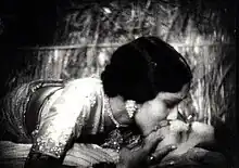 Devika Rani and Himanshu Rai are seen sharing a full-mouth kiss, with Devika Rani lying on the top.