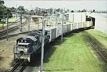 QR loco 2493 hauls a short container train across the Standard Gauge line to Sydney at Yeerongpilly station, 1987. Note the Standard Gauge loco shed in the background