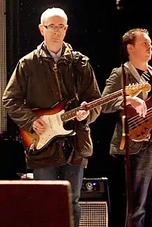 Dik Evans holding a guitar in front of a microphone stand