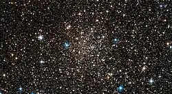 A loose scattering of small dull white dots on a black background with a few brighter coloured stars