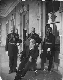 Three men in military uniforms standing around seated man