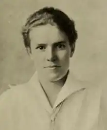 A young white woman, with short wavy hair, wearing a collared white blouse; she is looking directly at the camera