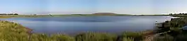 A lake with reeds and a hill beyond