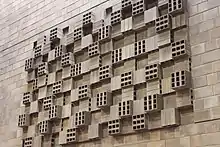 A sculpture on a wall of various boxes integrated into the brick