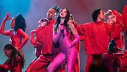 Dua Lipa performing in a pink catsuit surrounded by dancers in red outfits