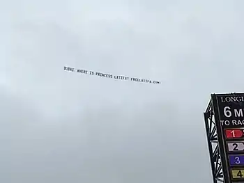 Top left corner of the video board at Churchill Downs, above it a banner against a cloudy sky, reading: DUBAI, WHERE IS PRINCESS LATIFA? FREELATIFA.COM