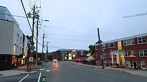 Two women walking on the sidewalk of a street with residential and commercial buildings on a summer evening.