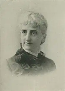 B&W portrait photo of an old woman with white hair in an up-do, wearing a dark high-necked blouse.