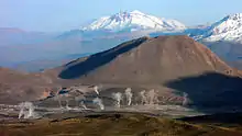 The steam plumes of the field at the feet of mountains, with higher snow-covered mountains far away