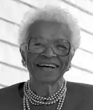 small back and white headshot of an older black woman smiling and looking at the camera. She has short white curly hair and is wearing glasses