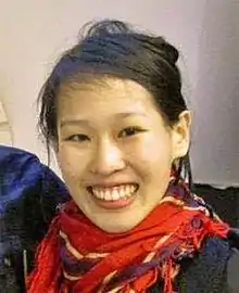 Lam, smiling, wearing a red scarf and black coat