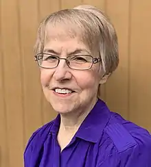 A portrait of Elizabeth Raum standing in front of a wooden door, taken in 2021.