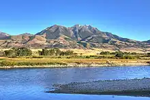 A river flows through a flat valley with mountains in the background.