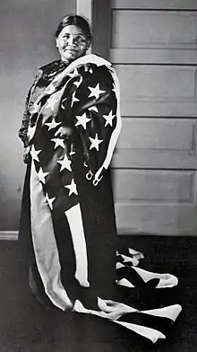 A stout woman in a dark blouse draped in an American flag.