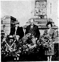 A black and white photograph of a group of people laying large flowery ceremonial wreaths at the base of a monument.