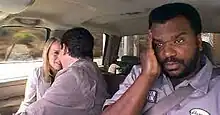 A white man and woman in business attire touch their foreheads smiling. A black man in a blue dress shirt holds his right hand against his forehead.