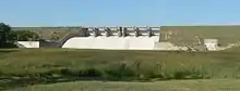 Concrete structure in grass-covered earthen dam; six floodgates