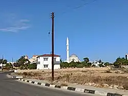 A white house with a red roof and a tower in the background. a road is running diagonally.