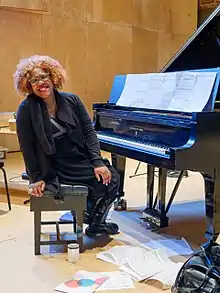 Wallen on a chair, leaning to look towards the camera, at a piano