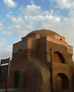 Mudbrick building with a domed roof and green entrance door with a sign outside in Farsi