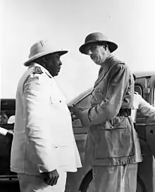 Éboué, a stout black man wearing white uniform and a pith helmet, faces Charles de Gaulle, a white man in similar but darker-colored uniform.