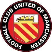 A circular badge with "Football Club United of Manchester" written in white capitals just inside the black circumference with a red trim. Inside is a yellow crest on a red background. The crest has a yellow ship with three sails on a white background, and three yellow stripes on a red background.