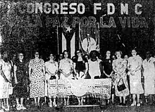 Group of 11 women standing behind a table below a banner proclaiming "For Life and For Peace"