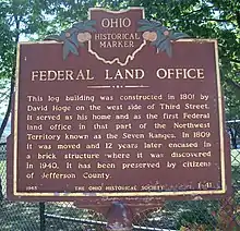 historical marker saying Federal Land Office This log building was constructed in 1801 by David Hoge on the west side of Third Street.  It served as his home and as the first Federal land office in that part of the Northwest Territory known as the Seven Ranges.  In 1809 it was moved, and twelve years later encased in a brick structure where it was discovered in 1940.  It has been preserved by the citizens of Jefferson County.