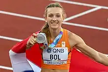 Photo of Femke Bol with a Dutch flag draped over one shoulder and holding a silver medal