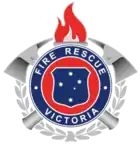 From a small silhouette of a brass firefighter's helmet rises a laurel wreath. Above it sits a shield of the Southern Cross, as in the Victorian coat of arms, encircled by the words FIRE RESCUE VICTORIA; behind this two crossed axes. A flaming torch surmounts the badge.