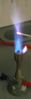 A flame with a small metal rod penetrating it; the flame near the rod is pale blue.