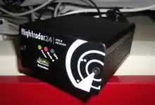 An ADS-B receiver, coloured black with the Flightradar24 logo, at a table.