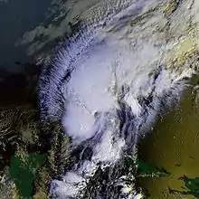 Satellite image of a minimal hurricane passing through the Florida strait. Two large areas of deep cloud cover make up most of the storm, with cirrus clouds extending to the northwest and sparse cloud cover to the northeast. The Yucatán Peninsula is seen at the bottom left, part of Cuba and Haiti are also at the bottom right.