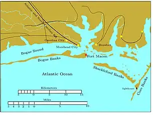 Bogue Banks is a long, narrow island extending from the left edge to past the middle of the chart. Fort Macon is at its eastern end. About two miles to the southeast is the western end of Shackleford Banks, which extends to the east southeast about seven miles. It is separated by a narrow inlet from Core Banks, which extends off the chart to the northeast. Behind these banks are the sounds, ranging in width from one to five miles. Carolina City, Morehead City, and Beaufort are sited on the sounds, all within 10 miles of Fort Macon. The Atlantic and North Carolina Railroad begins in Morehead City and runs off the map to the northwest.